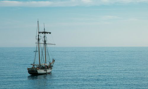 Single sailing vessel navigating calm open sea under clear sky