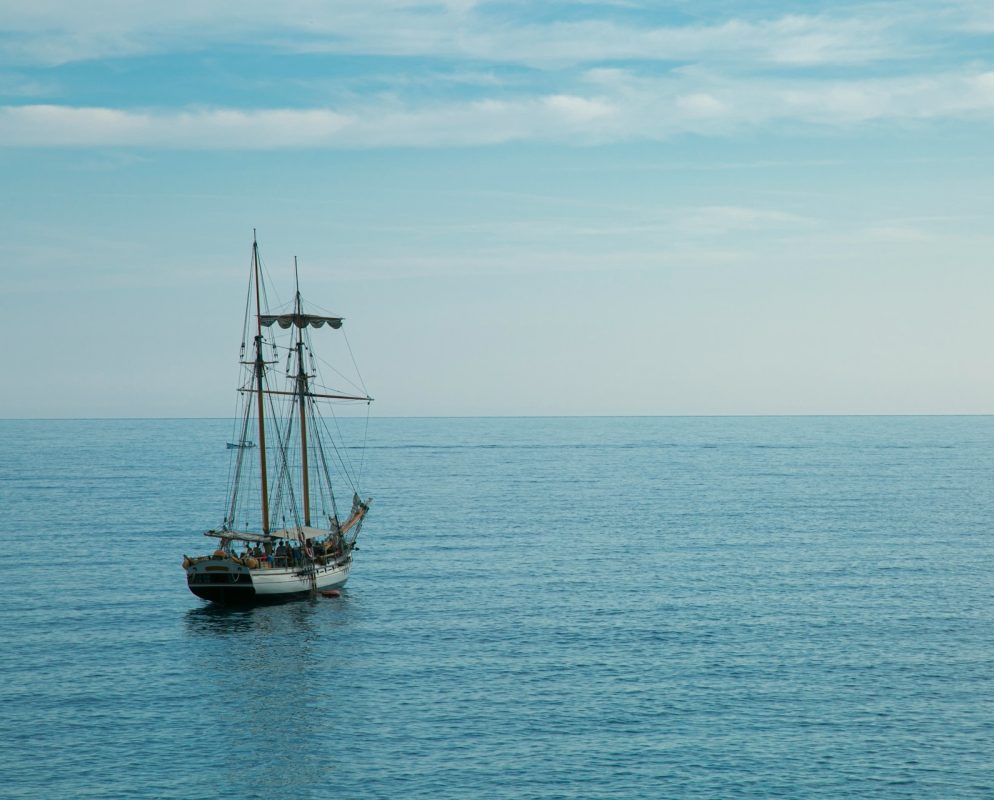 Single sailing vessel navigating calm open sea under clear sky