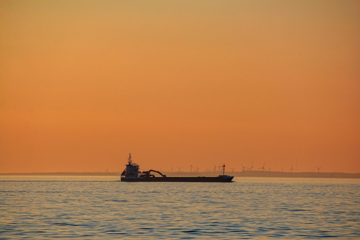 Oil tanker sailing at sea during sunset with wind turbines in background