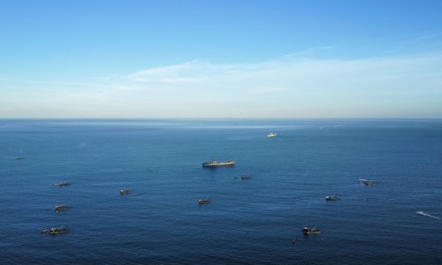 Ship and small boats at sea representing global shipping routes affected by maritime security concerns