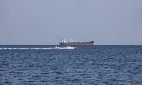 Cargo ship and speedboat in Strait of Hormuz showing maritime security risk and control of shipping route