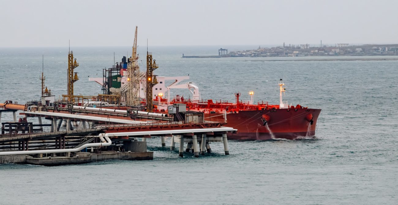 Oil tanker moored at petroleum storage terminal with large crude oil tanks