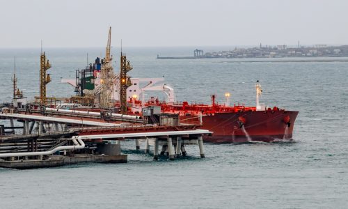 Oil tanker moored at petroleum storage terminal with large crude oil tanks