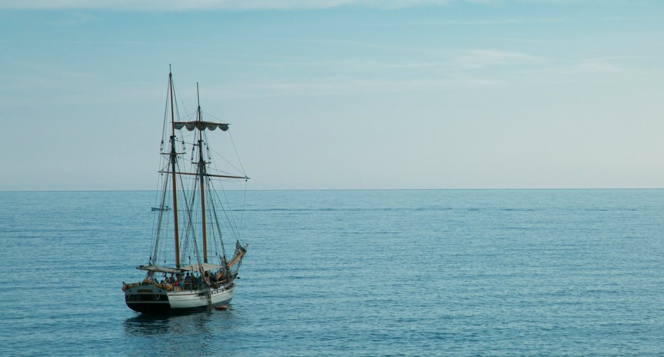 Single sailing vessel navigating calm open sea under clear sky