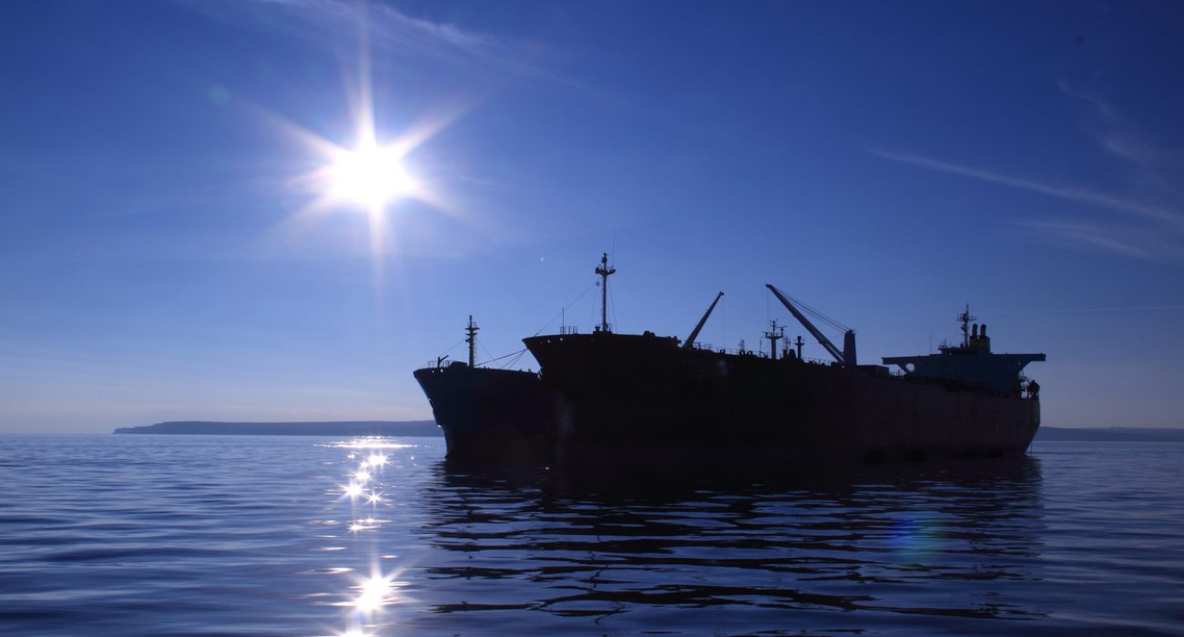Oil tankers anchored offshore illustrating global crude shipping and sanctions enforcement risk