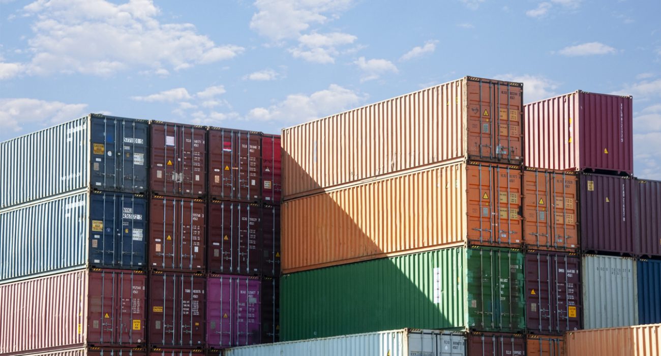 Stacked container shipping boxes at a port terminal representing global container trade and maritime logistics
