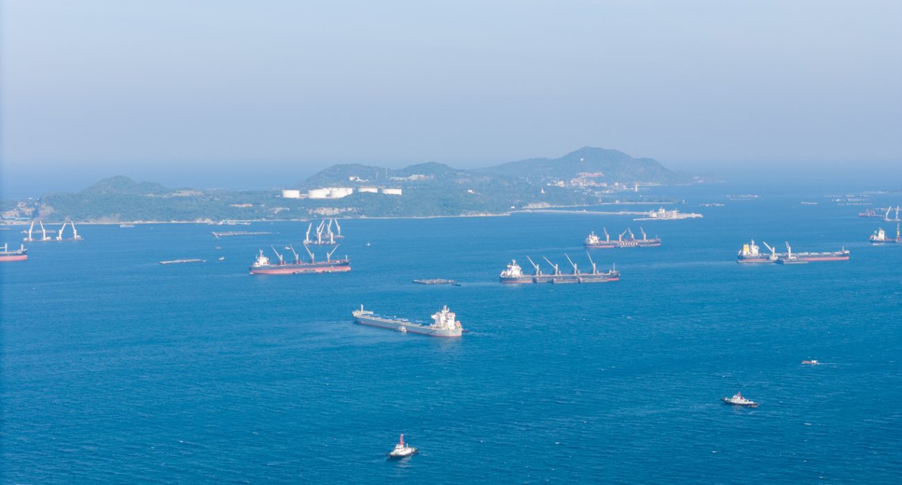 Cargo ships and oil tankers anchored at sea representing delays in global shipping routes