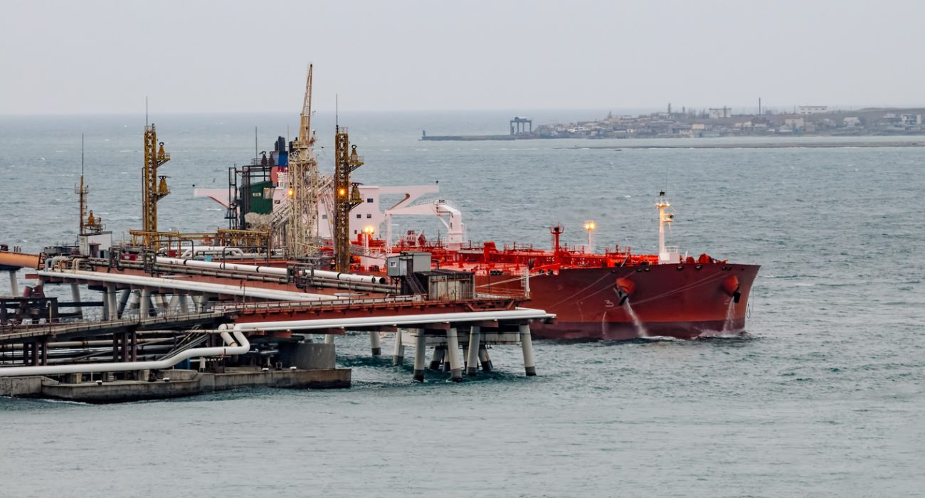 Oil tanker moored at petroleum storage terminal with large crude oil tanks