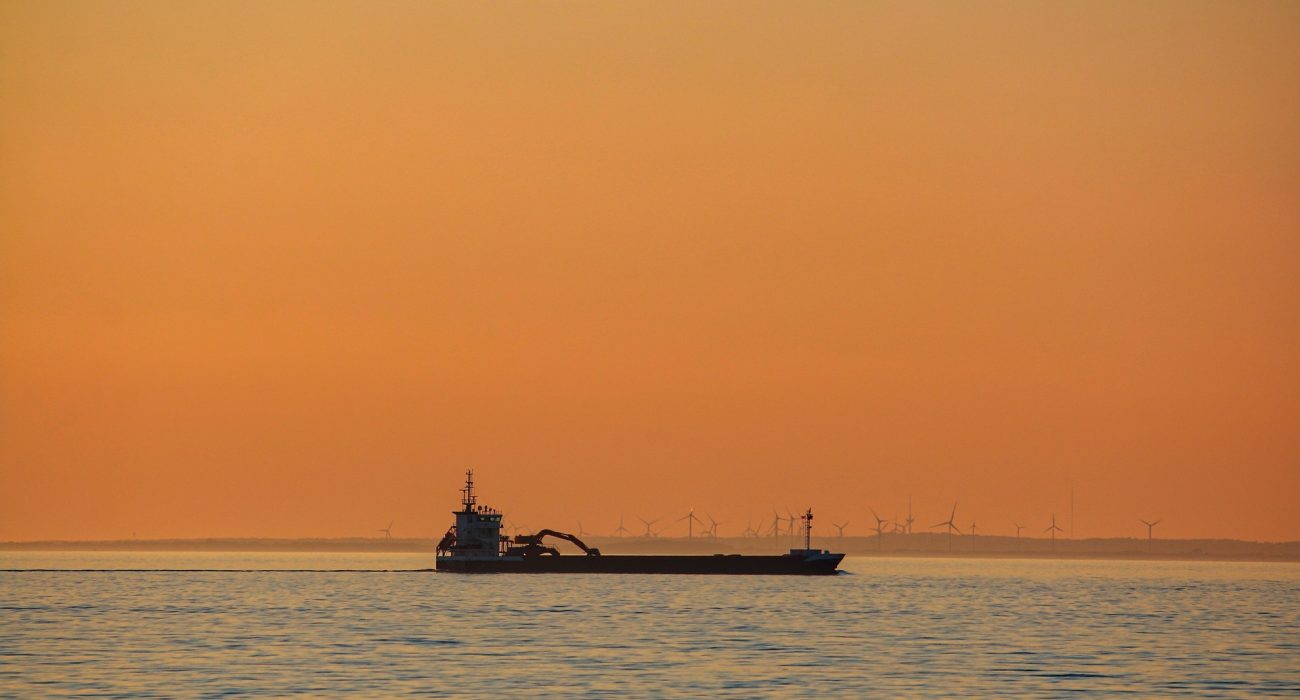 Oil tanker sailing at sea during sunset with wind turbines in background